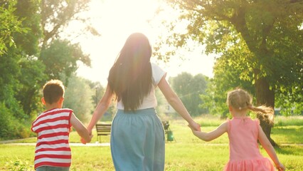Mother and children run in park amidst serene embrace of nature. Mother with children hand in hand runs in display of familial joy. Mother and children run with joined hands under embrace of sunlight