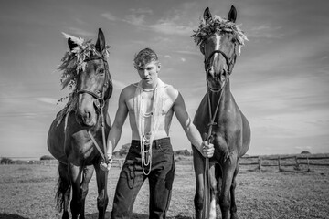 jeune homme tenant deux chevaux avec des couronnes de fleurs en noir et blanc - obrazy, fototapety, plakaty