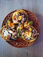 Delicious dish of Sopes and seafood tostadas that are a fried tortilla with beans, shrimp and octopus on top