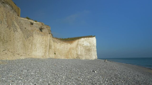 Blue sea gently lapping against rocky shore beneath magnificent white cliffs. Picturesque coastline with chalk sea cliffs topped with grass stretching along ocean in southern England on a sunny day.