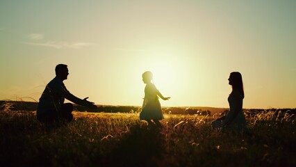 Parents with child playing after delightful picnic on nature in field at sunset. Parents hugging...