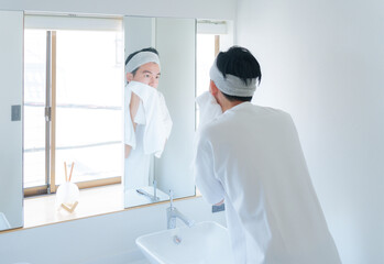 洗顔した顔をタオルで顔を拭く若い男性