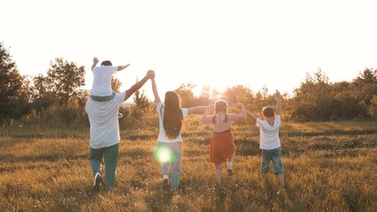 Strong friendly family with children walks raising hands across meadow at sunset time. Loving...