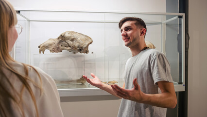 Curious young people observing animal skeletons and skulls displayed in a showcase during natural...