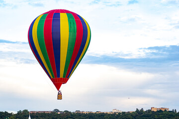 Multi colored balloon flying high in the sky over the city. Balloon basket with people. Burning gas. Romantic trip. Copy space