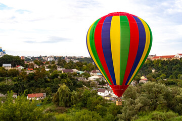 Multi colored balloon flying high in the sky over the city with a lot of trees. Balloon basket with people. Romantic trip. Copy space