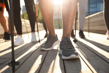 Group of people practicing Nordic walking with poles outdoors on sunny day, closeup