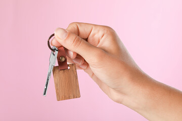 Woman holding key with wooden keychain on pink background, closeup - Powered by Adobe