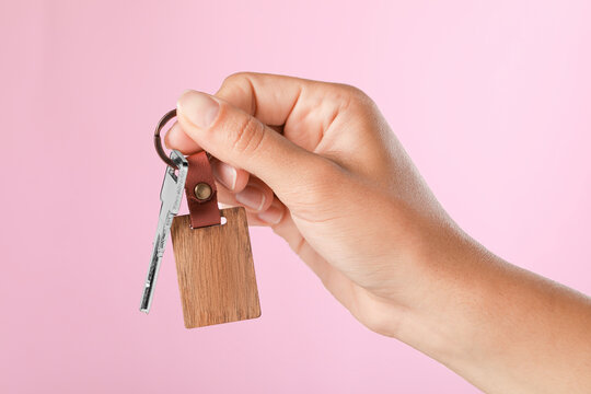 Woman holding key with wooden keychain on pink background, closeup
