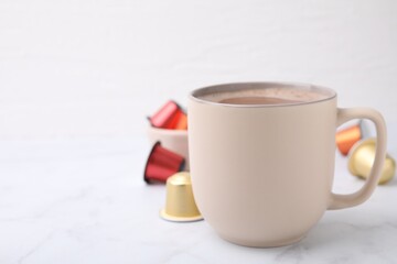 Cup of coffee and capsules on white marble table, closeup. Space for text