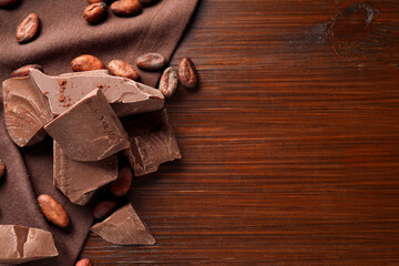 Pieces of tasty milk chocolate and cocoa beans on wooden table, flat lay. Space for text