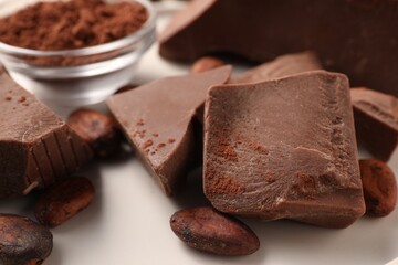 Pieces of tasty milk chocolate and cocoa beans on white table, closeup