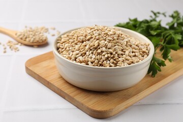 Dry pearl barley in bowl on white tiled table, closeup
