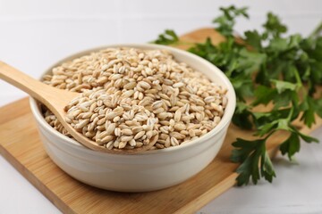 Dry pearl barley in bowl and wooden spoon on table, closeup