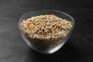 Dry pearl barley in bowl on dark gray table, closeup