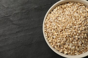 Dry pearl barley in bowl on dark gray table, top view. Space for text