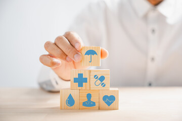Symbolic image, Hand holds wooden block displaying healthcare and medical icons. Portrays safety, health, and family well-being, symbolizing pharmacy, heart care, and happiness. health care concept