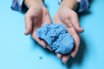 Woman playing with kinetic sand on light blue background, closeup