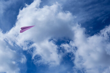 Naklejka na ściany i meble Violet paper plane flying in blue sky with clouds