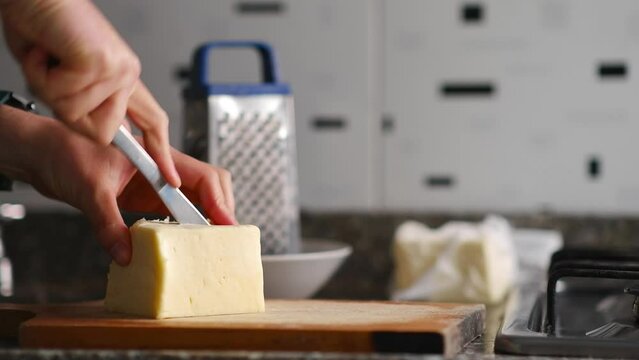 Two hands cut mozzarella cheese on cutting board near food scraper and white plate, horizontal video