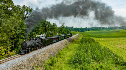 An Aerial View of a Narrow Gauge Steam Passenger Train, Approaching Traveling Thru Farmlands, Blowing Smoke, on a Sunny Summer Day