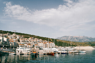 Fototapeta na wymiar Motor and sailing yachts are moored off the coast of Lustica Bay against the backdrop of colorful villas. Montenegro