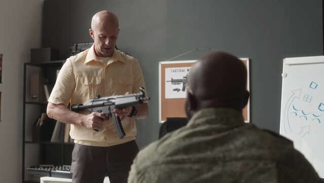 Rear view of unrecognizable male cadet answering during class and professor teaching how to use submachine gun in service academy