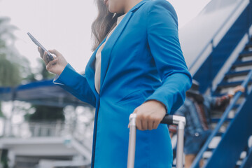 Young asian woman in international airport, using mobile smartphone and checking flight at the flight information board