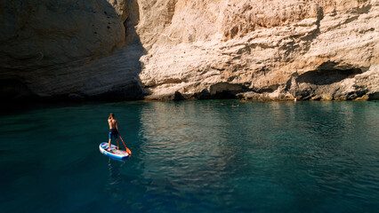 View of surfer on board in turquoise water in front of big cliff