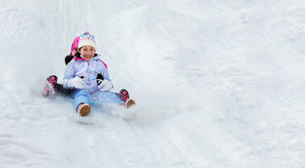 Little girls are sledding down snow slide. Having fun in the winter, fun vacations.