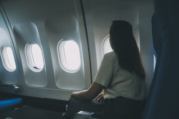 Silhouette of woman looks out the window of an flying airplane. Passenger on the plane resting...