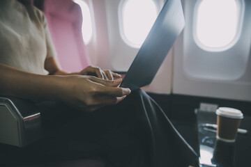 Asian woman passenger sitting in airplane near window and reading news from social networks or...
