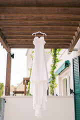 Bride dress hangs on a hanger on a wooden cover on the hotel terrace
