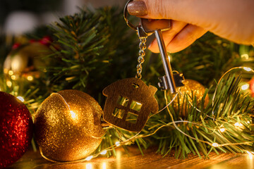 Gift key house with a keychain in hand backdrop of Christmas tree. Building, design, project,...