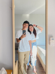 Young Asian couple taking selfie in mirror with mobile phone in the bedroom
