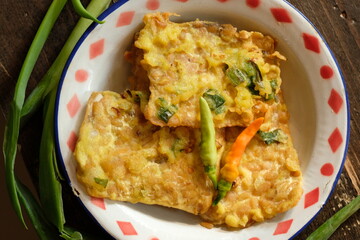 Tempe Mendoan is Tempeh is thinly sliced tempeh then coated with seasoned flour and fried. Indonesian food. Served on vintage plate. 