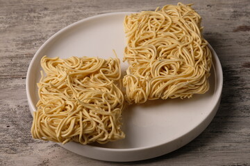 dry noodles on a white ceramic plate. on a gray rustic wooden table. Dry noodles are raw noodles made from wheat flour, eggs, preservatives. chinese food. carbohydrate. mie kering mentah. mie instan. 