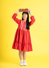 full body Image of an Asian girl holding a gift box and wearing a dress posing on a yellow background

