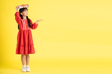 full body Image of an Asian girl holding a gift box and wearing a dress posing on a yellow background
