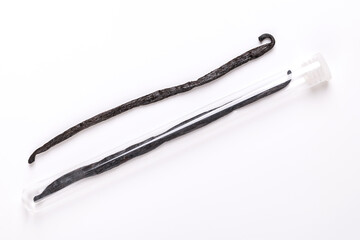 Two whole vanilla pods. Dried, dark brown and ripe beans, fruits of Vanilla planifolia. One of the beans kept in a glass tube with plastic plug. Spice with distinctive flavor, used for food flavoring.