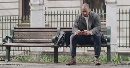 Serious, casual and relaxed man typing text on phone, browsing social media and checking notifications while sitting on a bench in a park. Male entrepreneur and guy reading and replying to emails