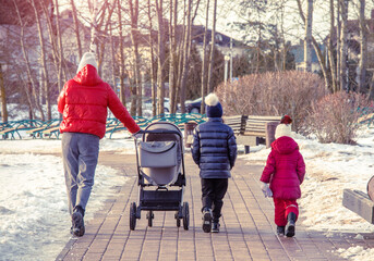 A woman with two daughters and a baby carriage in a winter park
