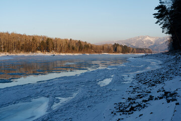 Siberia. A freezing river with ice floes against the backdrop of forest and mountains.