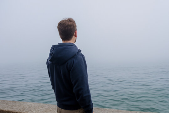 guy at sea. a young guy stands on a bridge near the sea with fog, rear view, against the backdrop of a large dark sea with white fog