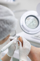 Grinding the thumb with a close-up milling cutter. A female podiatrist does a hardware pedicure.