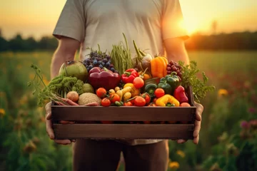 Rolgordijnen Human holding wooden box of different vegetables on field in sunset. Generative AI © Suttida