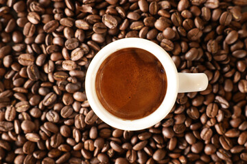 A view looking directly down on a white espresso cup filled with a freshly brewed coffee shot with brown crema. Background of roasted coffee beans.