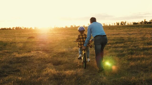 Affectionate papa actively involved in assisting little kid on riding bicycle. Caring dad prevents mishaps holding bike of son. Father provides risk-free bike ride for beloved child in field