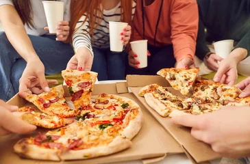 Foto op Plexiglas Close up hands of a young people friends gathering in pizzeria or at home together eating tasty Italian food taking pizza slices from box enjoying party with cardboard cups in hands. © Studio Romantic