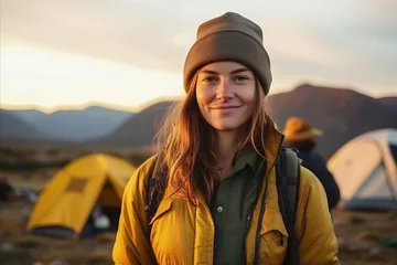 Poster Beautiful young woman hiker standing in front of her tent at sunset © igolaizola